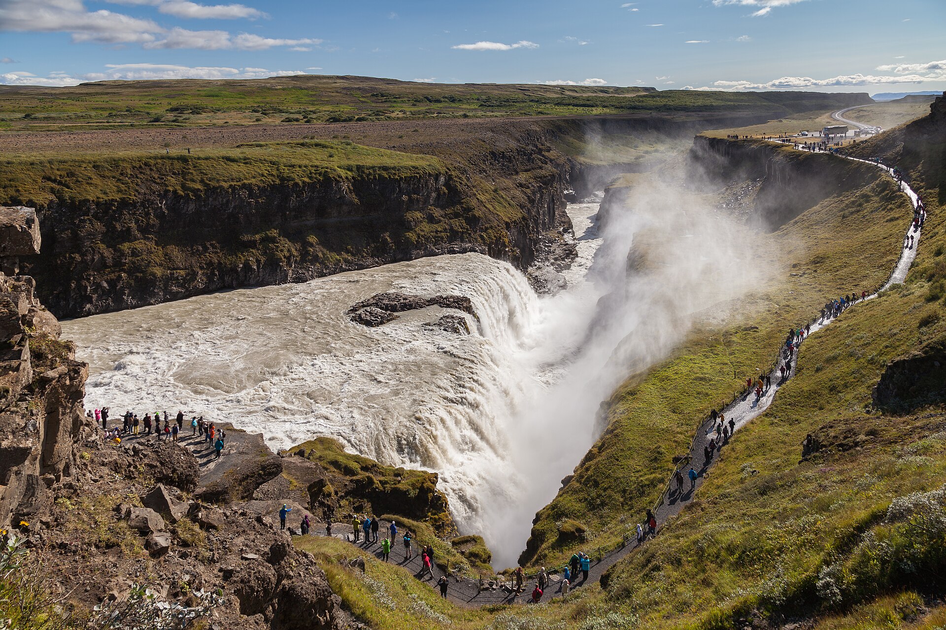Gullfoss waterfall tumbling into its canyon, with a path of visitors along the green rim.
