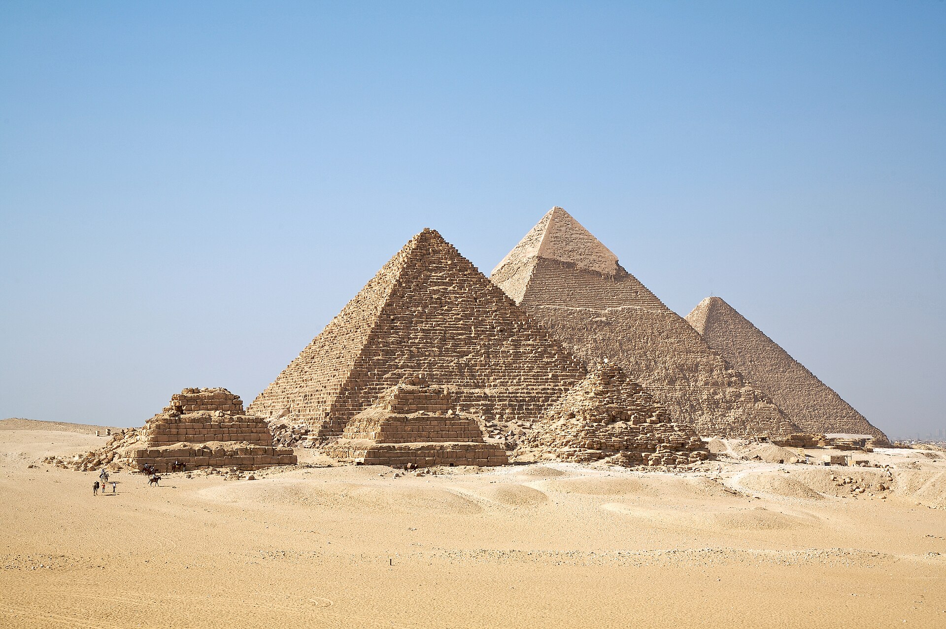 The pyramids of Giza standing in a row on the desert plateau under a pale blue sky.