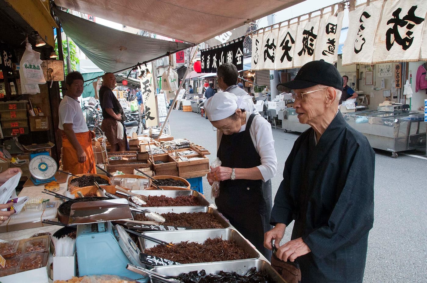 Stall holders and early shoppers among the awnings and banners of the Tsukiji market lanes in Tokyo.