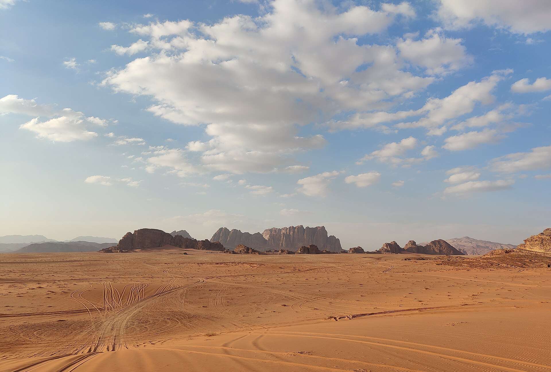 Open red sand and isolated sandstone mountains under a big sky in the Wadi Rum desert, Jordan.