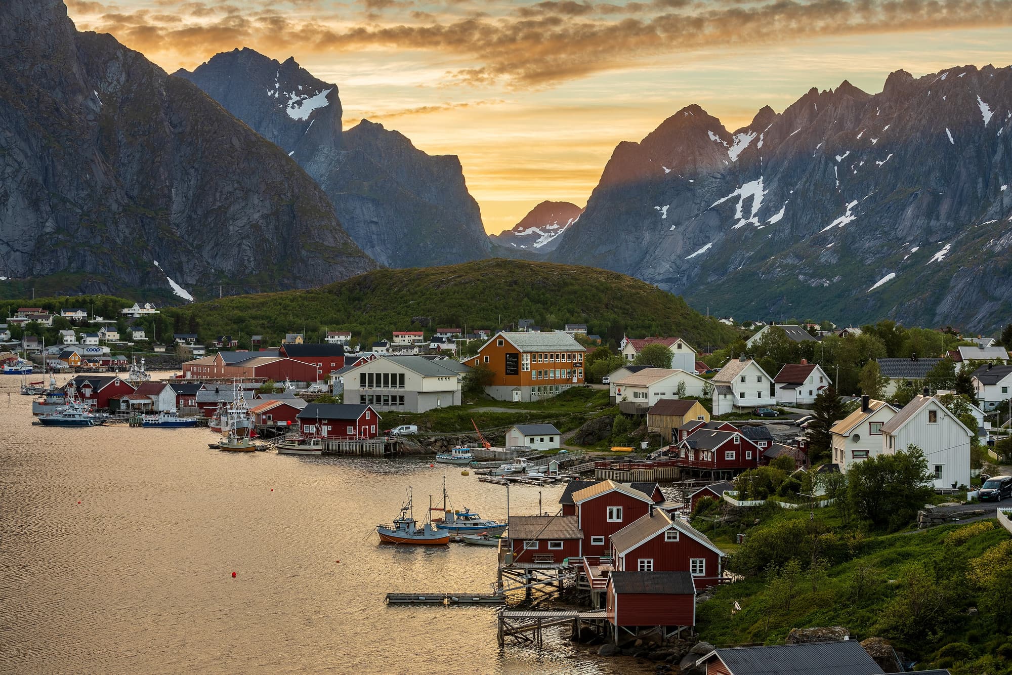 Red and white timber houses of Reine on the shore of Reinefjorden in Lofoten, with granite peaks behind the village.