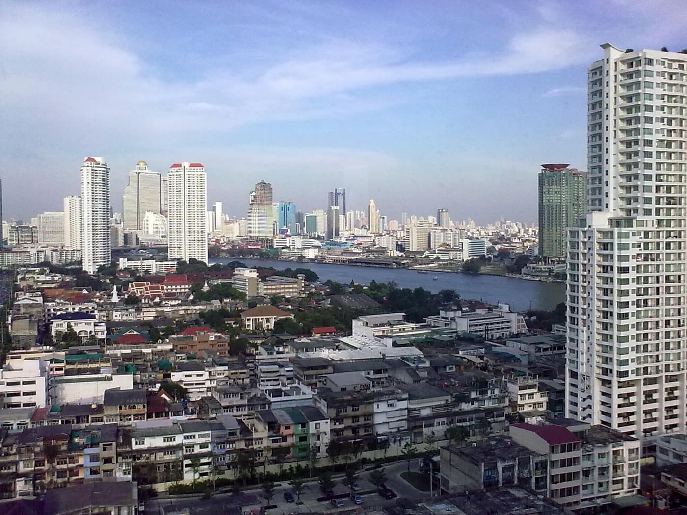 High-rise towers of Bangkok along a bend of the Chao Phraya river, seen from above the riverside rooftops.