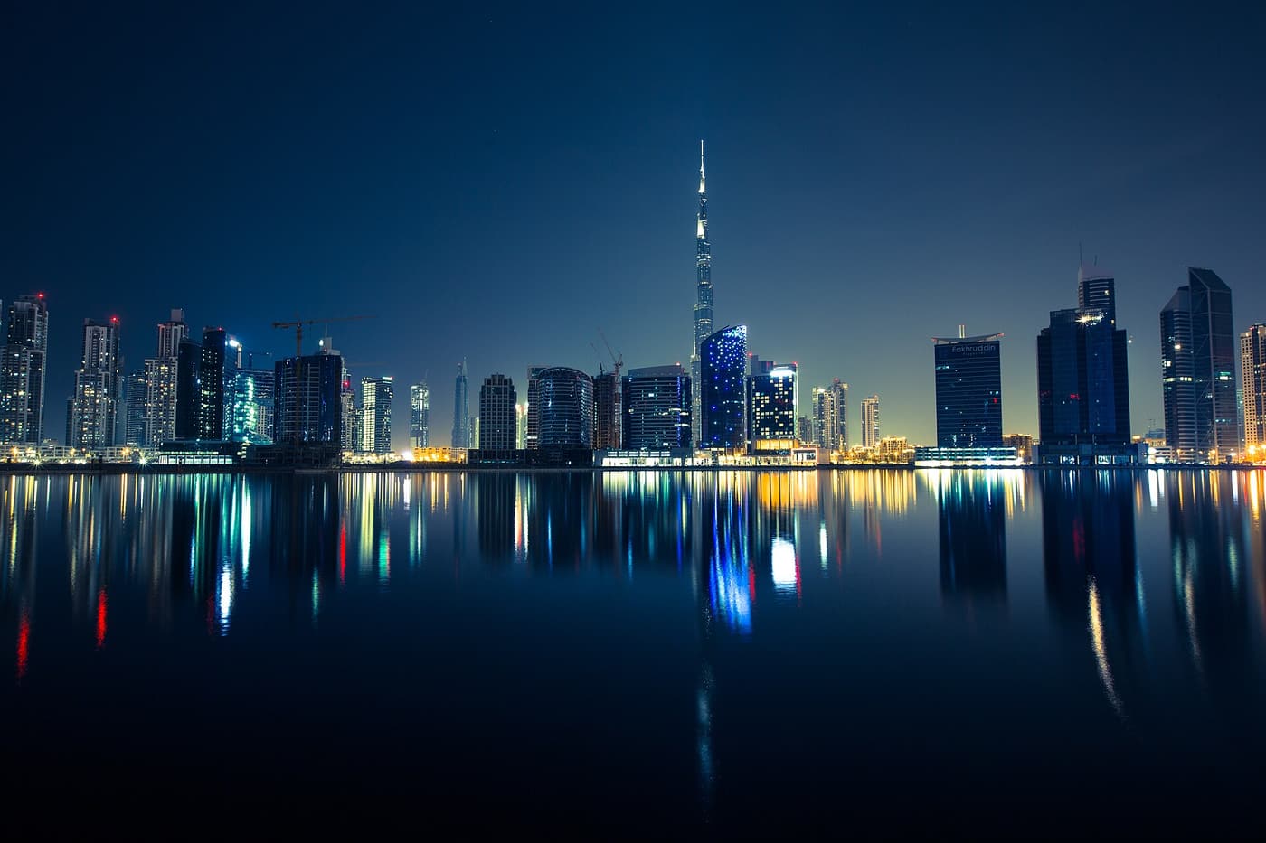 The Downtown Dubai skyline at night with the Burj Khalifa, reflected in still water.