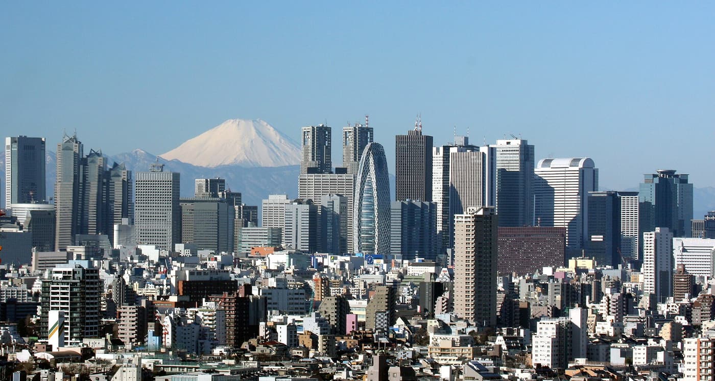 The Shinjuku skyscraper cluster in Tokyo on a clear day, with snow-capped Mount Fuji behind it.