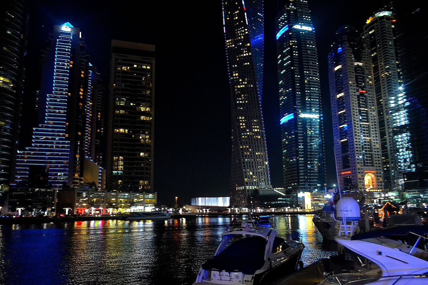 Lit towers of Dubai Marina at night, with motor yachts moored in the foreground.