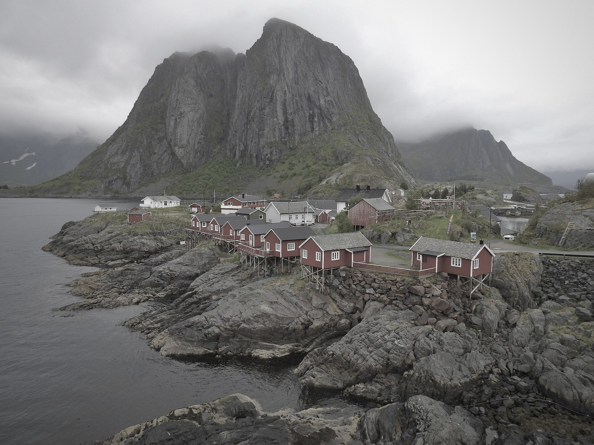 Red rorbu cabins of Hamnøy in Lofoten below a steep grey mountain wall.