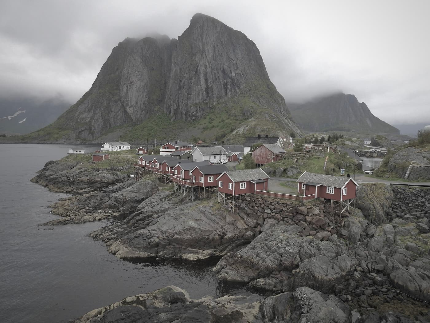 Red rorbu cabins of Hamnøy in Lofoten below a steep grey mountain wall.