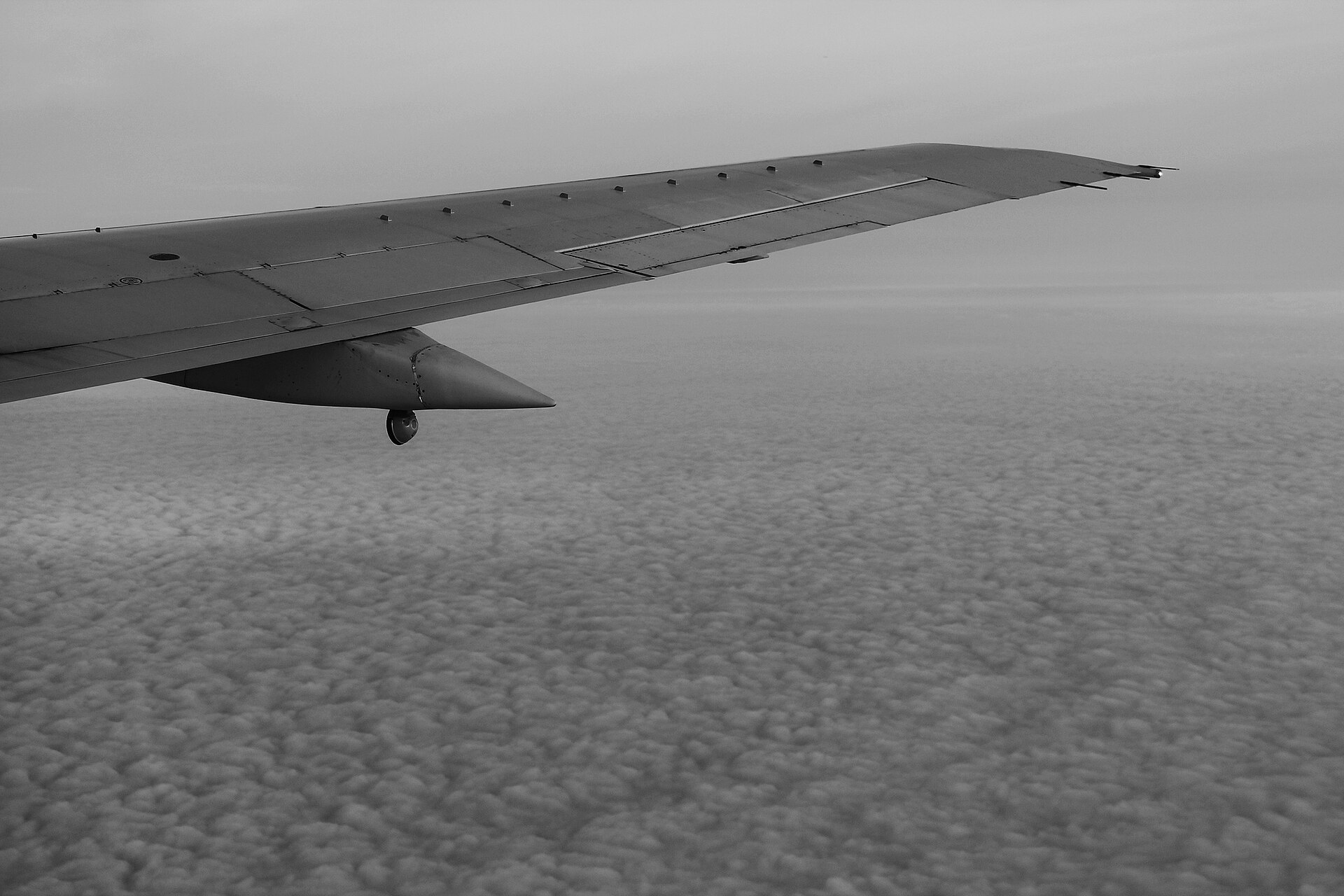 The wing of an airliner above a field of small scattered clouds.